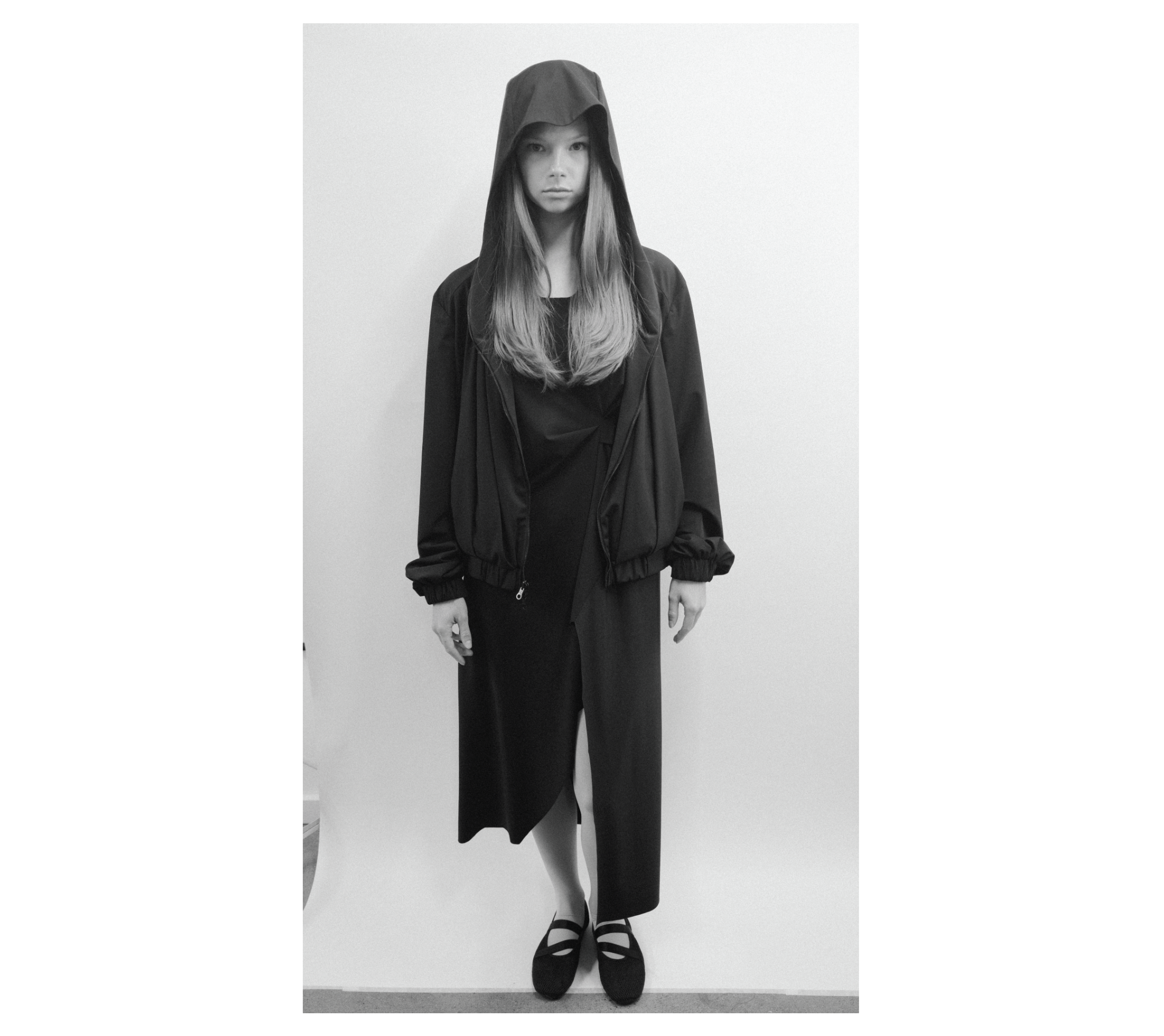 Black and white fashion image of a person wearing a hooded outfit.